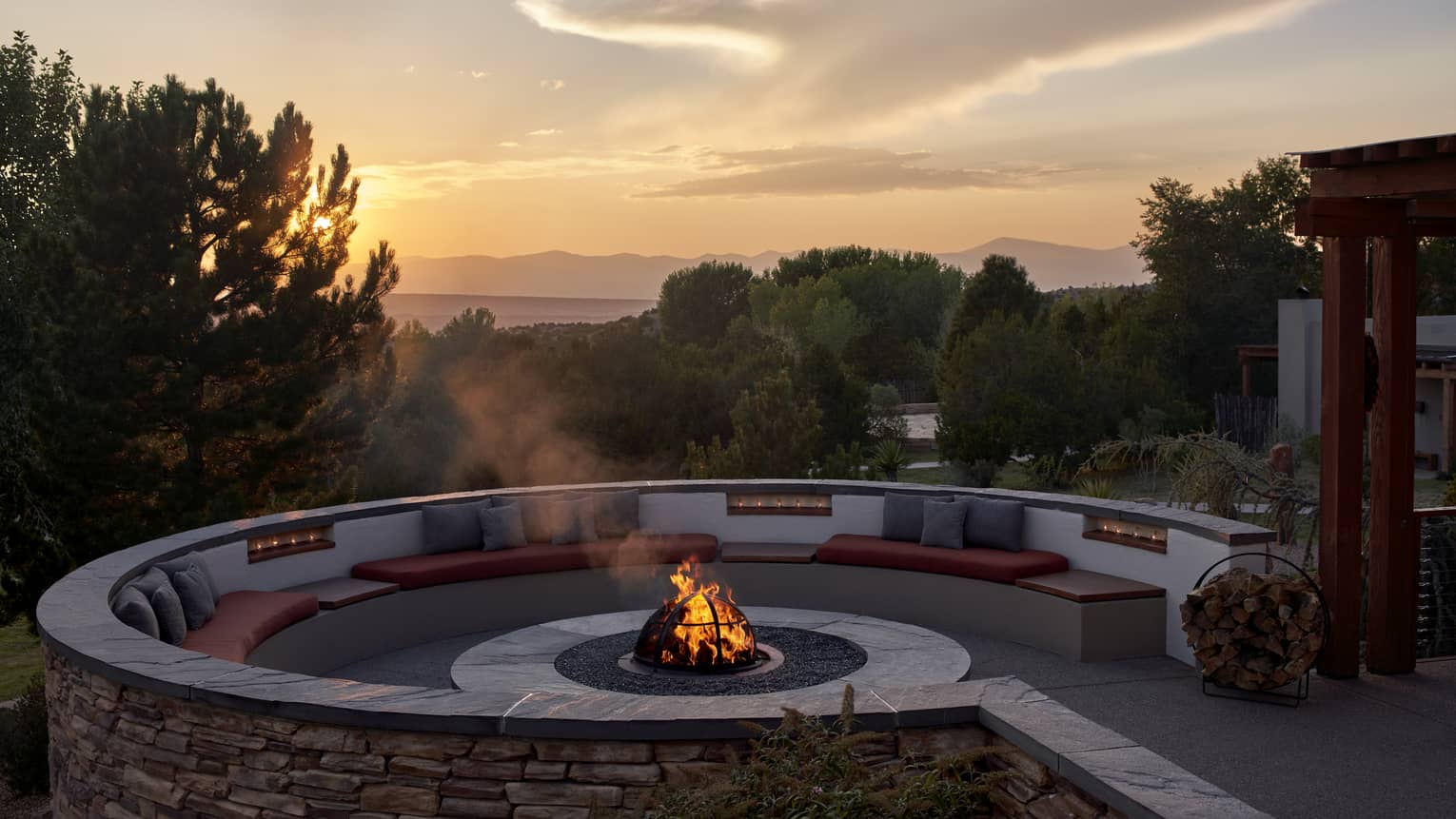 A firepit outside during a sunrise, surrounded by trees and plants.