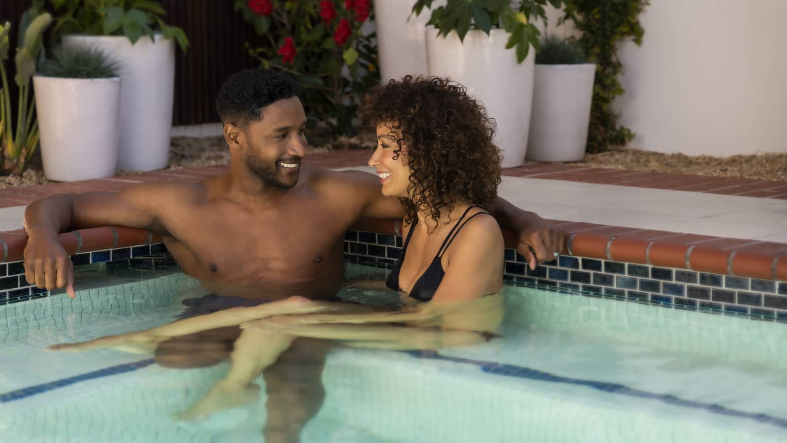 A man and woman relaxing in a pool together and talking.
