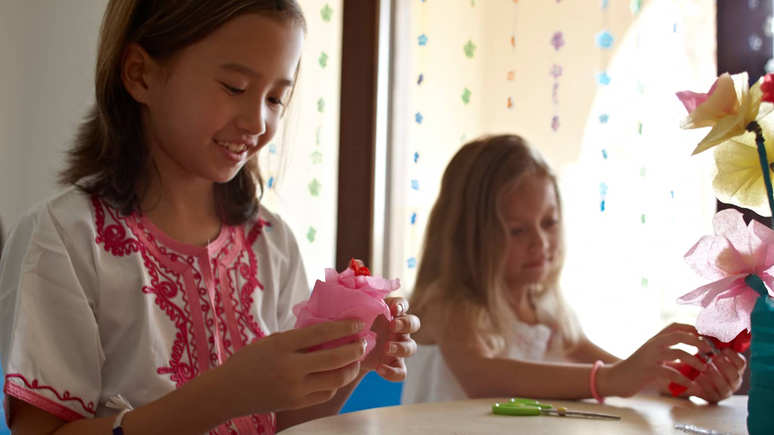 Two young girls at craft table with pink tissue paper