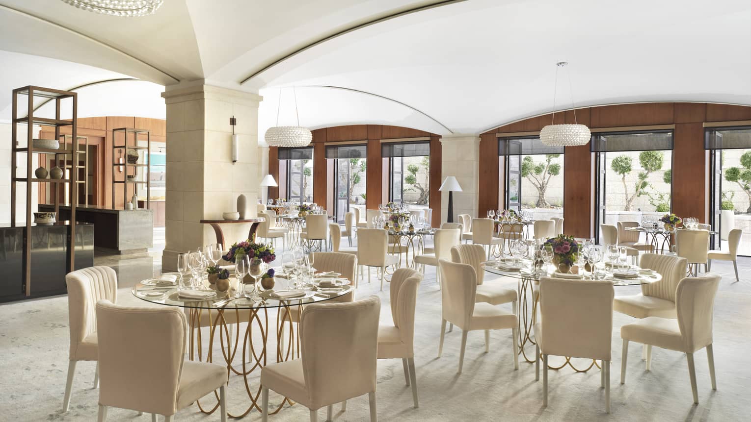 A series of cream coloured chairs surrounding glass tables with iron legs.
