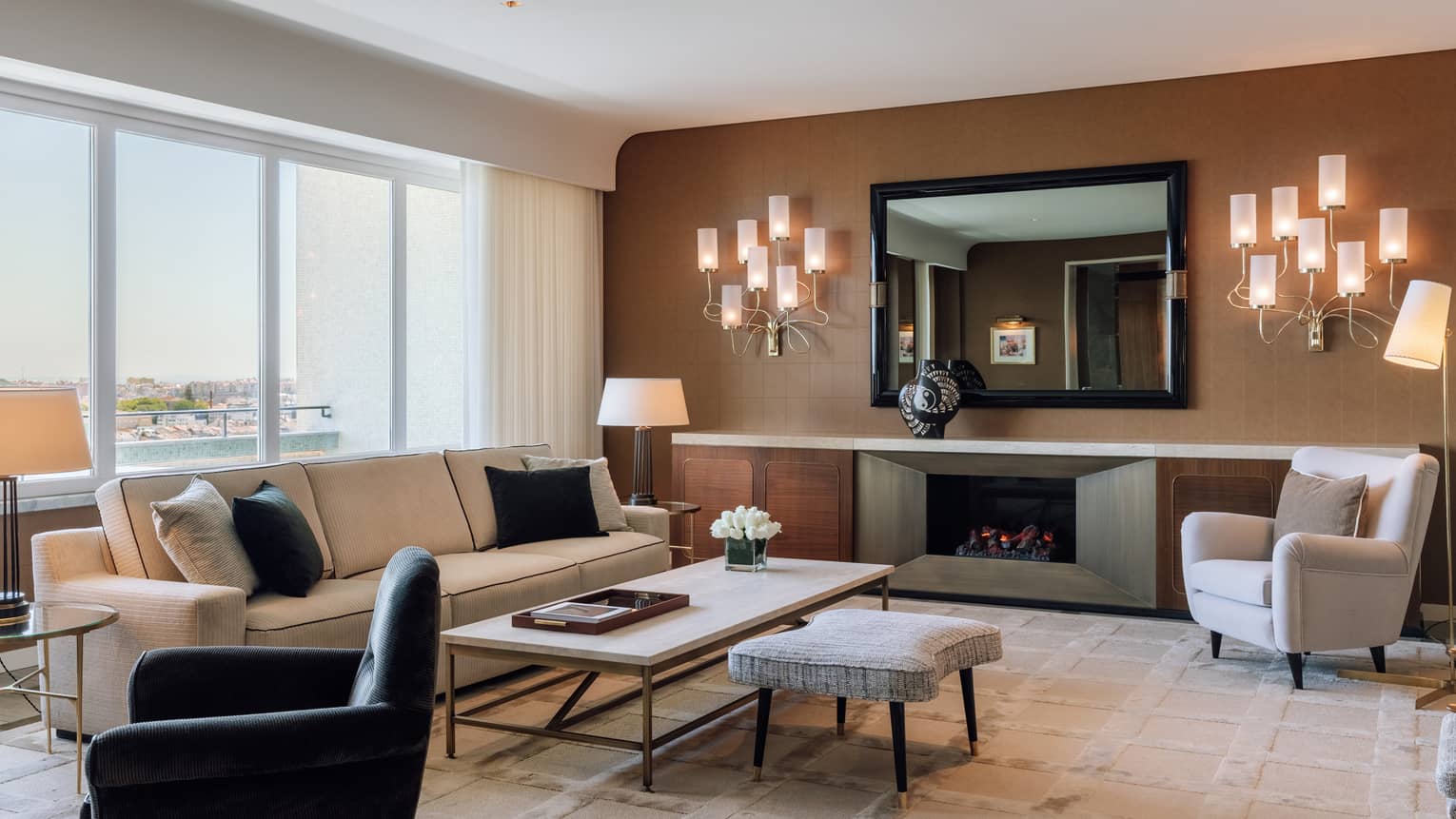 Stylish hotel living room with a sofa, armchairs, coffee table, fireplace and large windows with a city view.