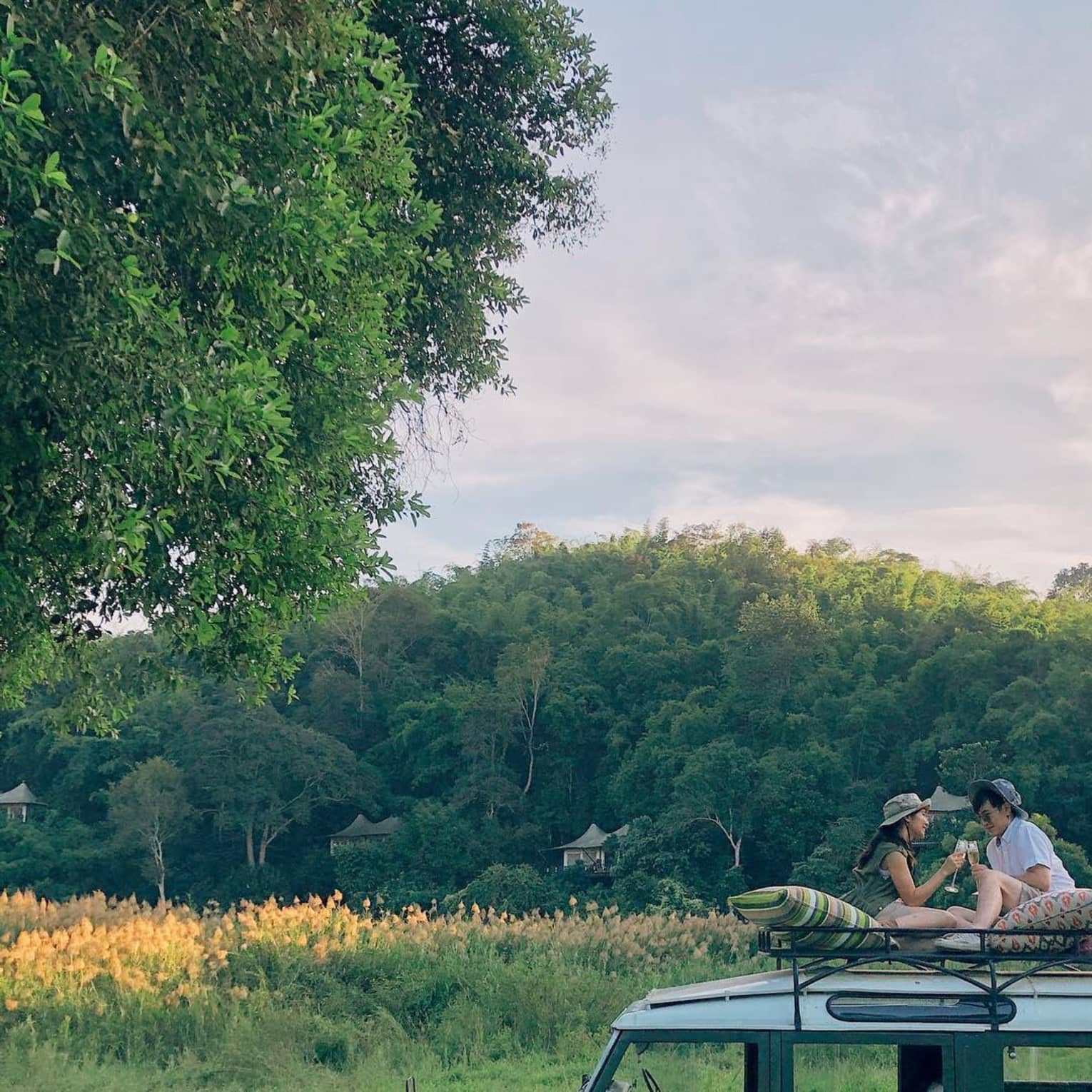 Two guests sit on top of a safari vehicle in a field