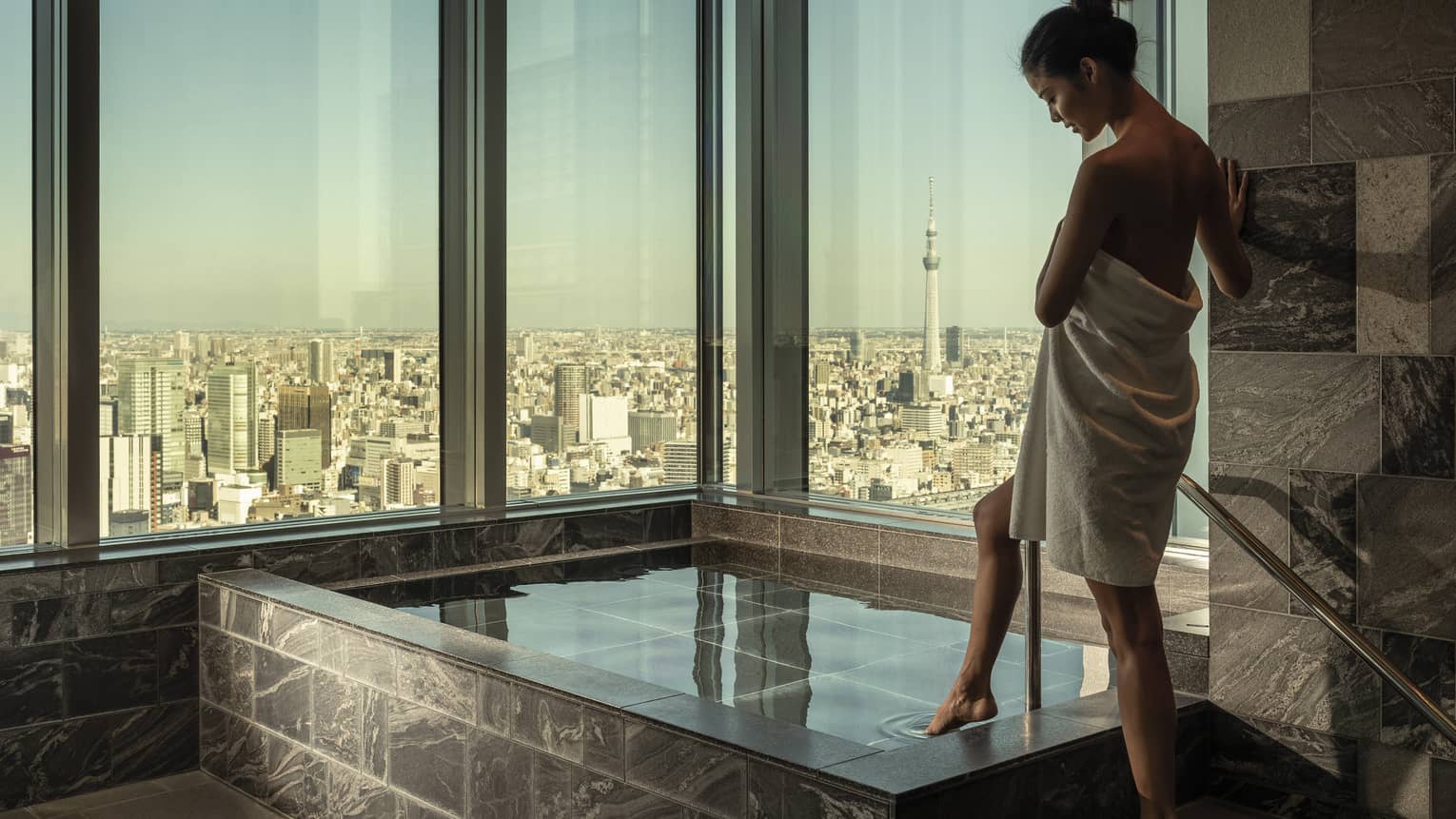 Woman wrapped in white towel dips her toe into the ofuro bath