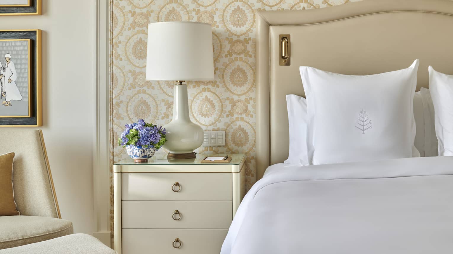 Bed with white sheets and Four Seasons-embroidered sham, nightstand and lamp