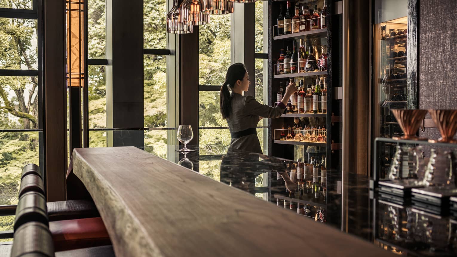 Lounge bartender retrieves bottle on wine from cellar behind long rustic wood bar
