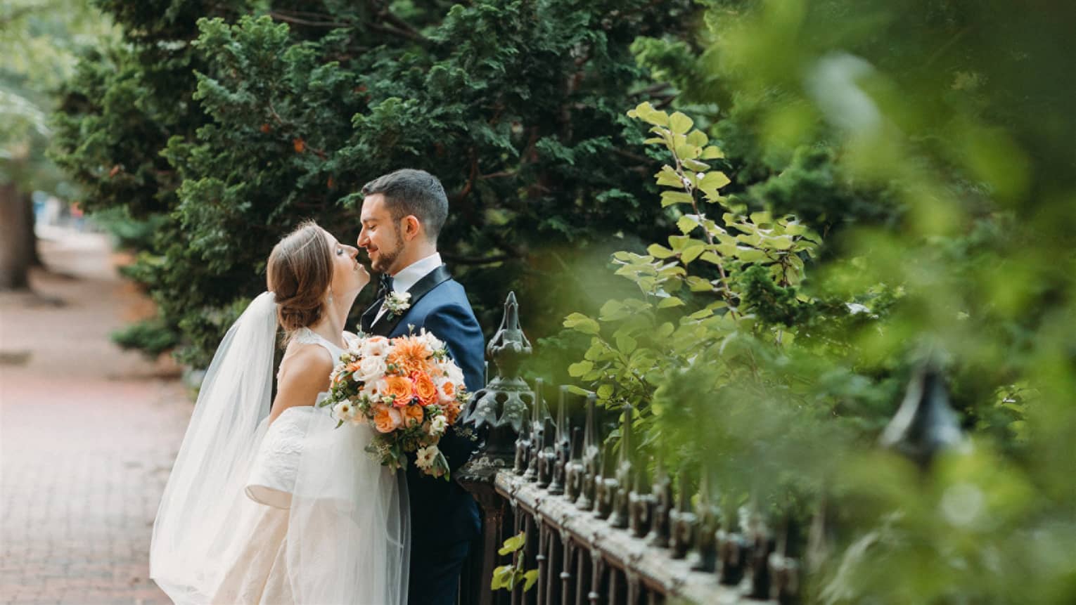 A bride and groom embrace on a city street surrounded by trees