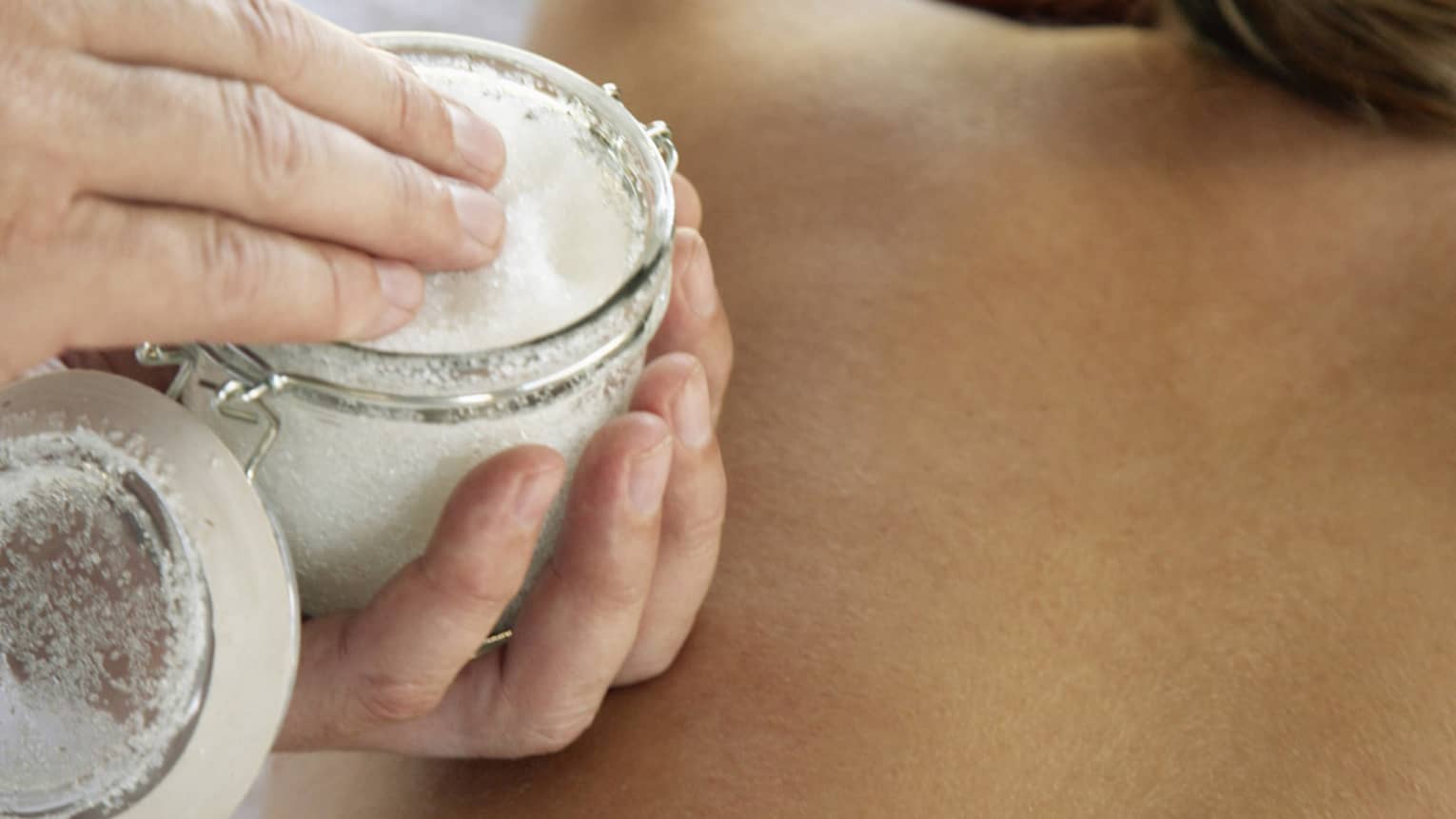 Jar of sea salt scrub above woman's bare back in spa