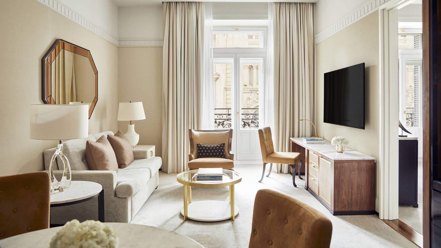 Four Seasons suite living area with beige sofa, brown leather armchair, console table with chair, wall-mounted TV, round glass coffee table and elegant decor