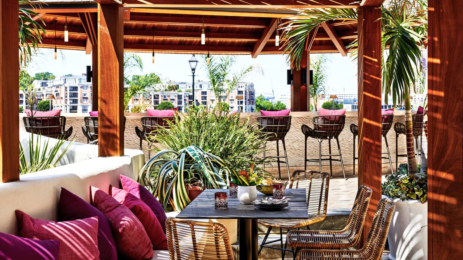An outdoor eating venue with red cushions on benches and stools surrounded by red pillars and trees.