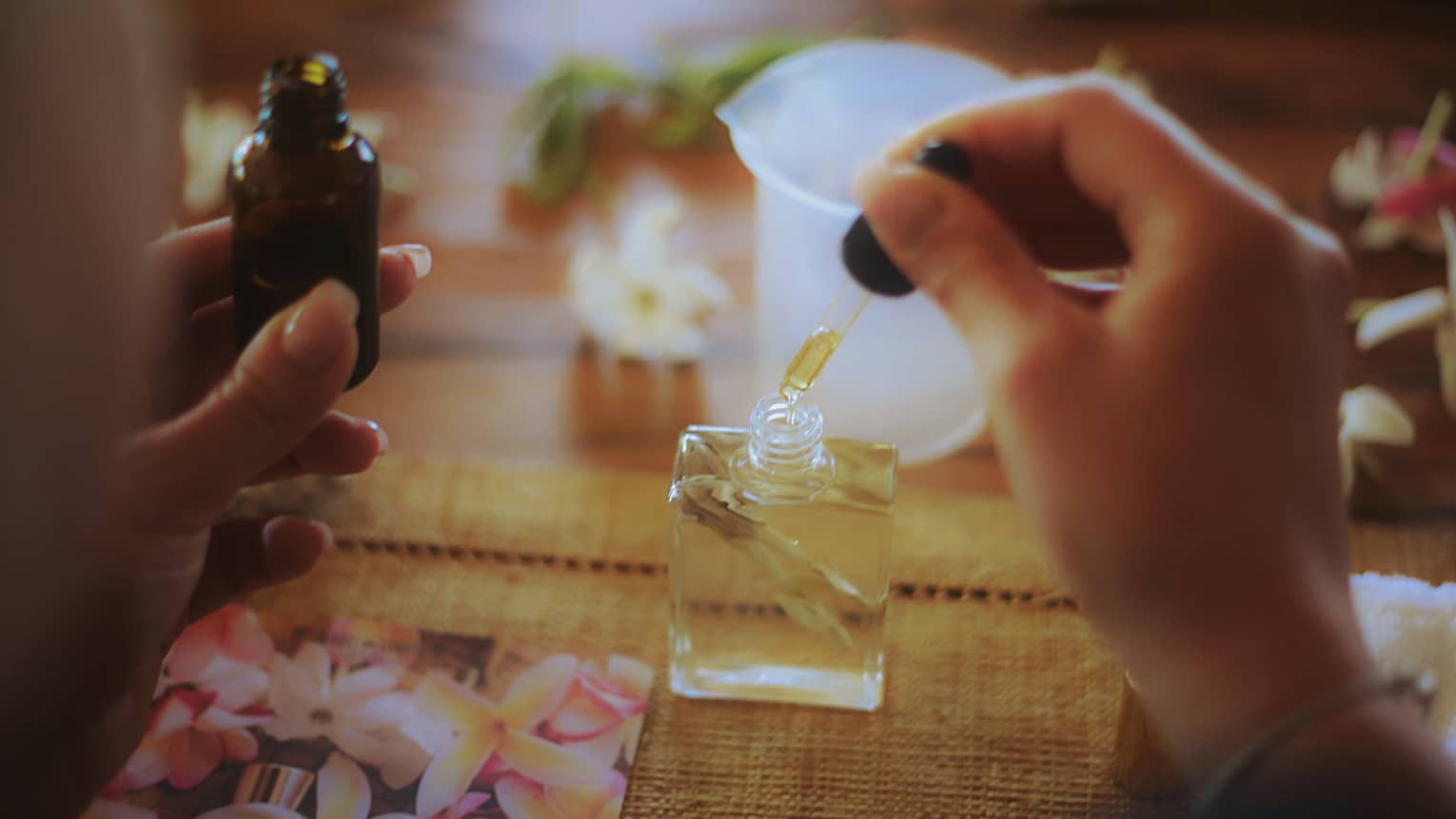 Person uses eyedropper to dispense monoï oil into a bottle