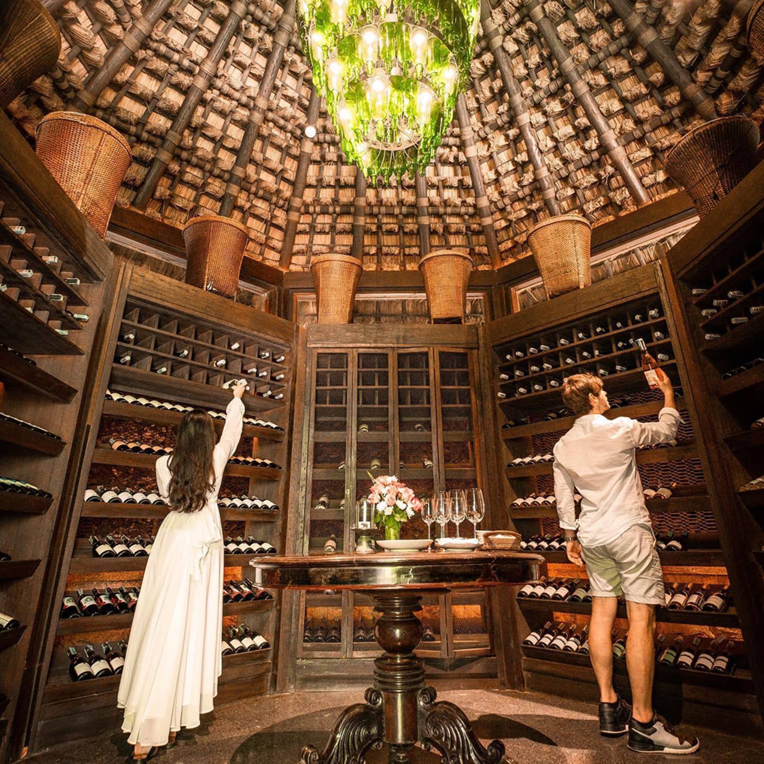 Man and woman select bottles of wine from walls of dome shaped cellar under chandelier