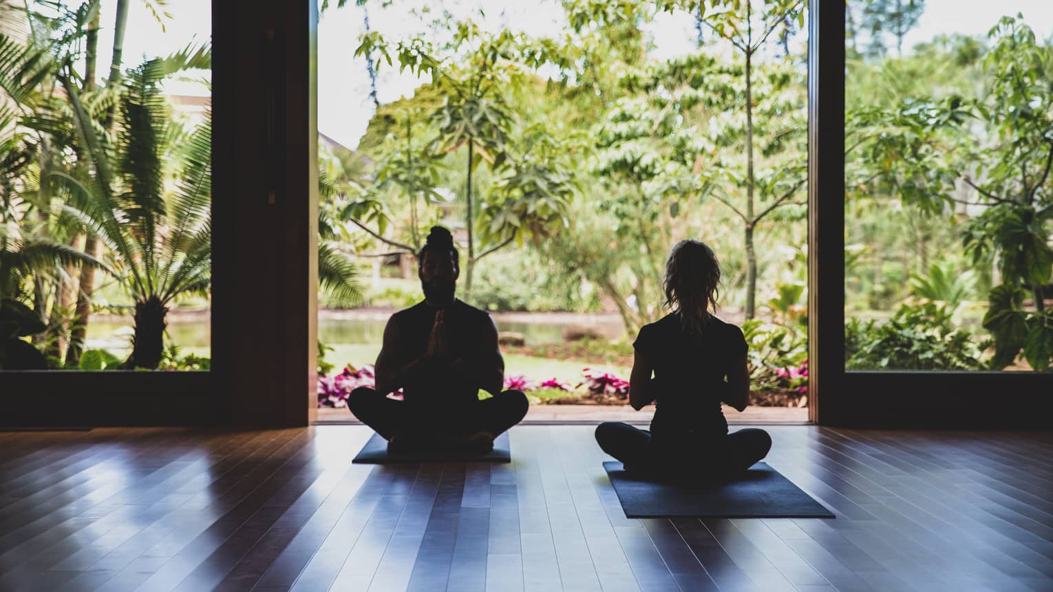Two people practice yoga in the outdoor covered pavilion surrounded by greenery
