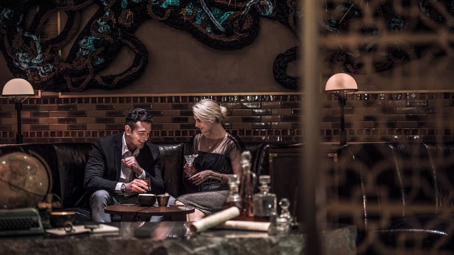 Man, woman drink cocktails on dark leather lounge sofa in Charles H lounge