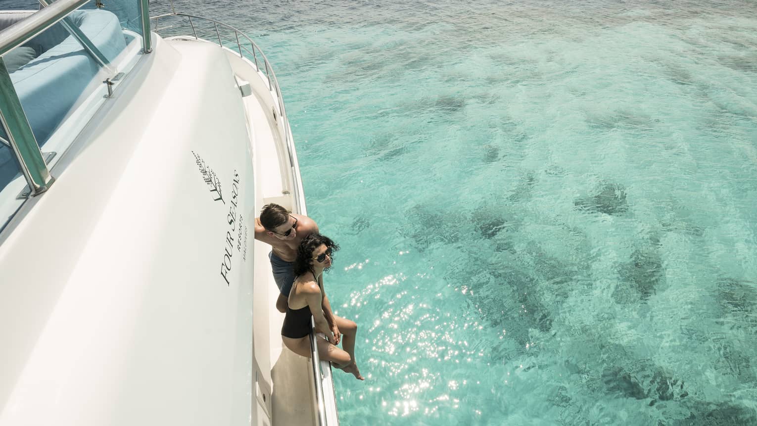 A couple lounges on the side of a yacht in a blue lagoon