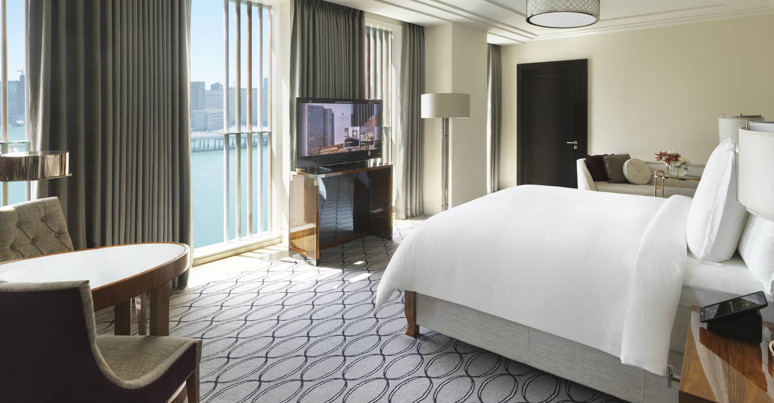 Hotel room with king bed, table with two chairs, TV and wall of windows