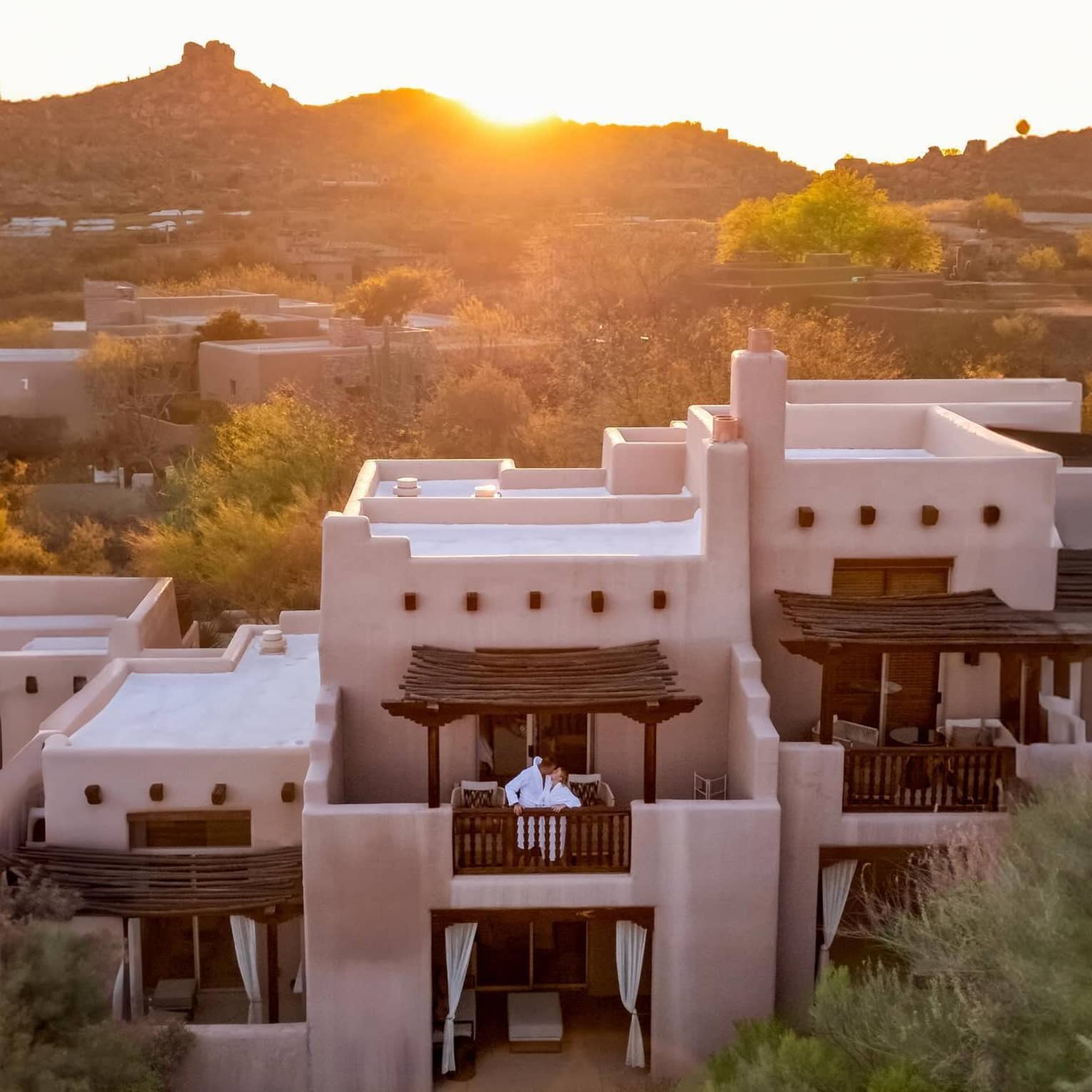 Aerial view of a couple standing on a balcony with a mountain view behind them at sunset
