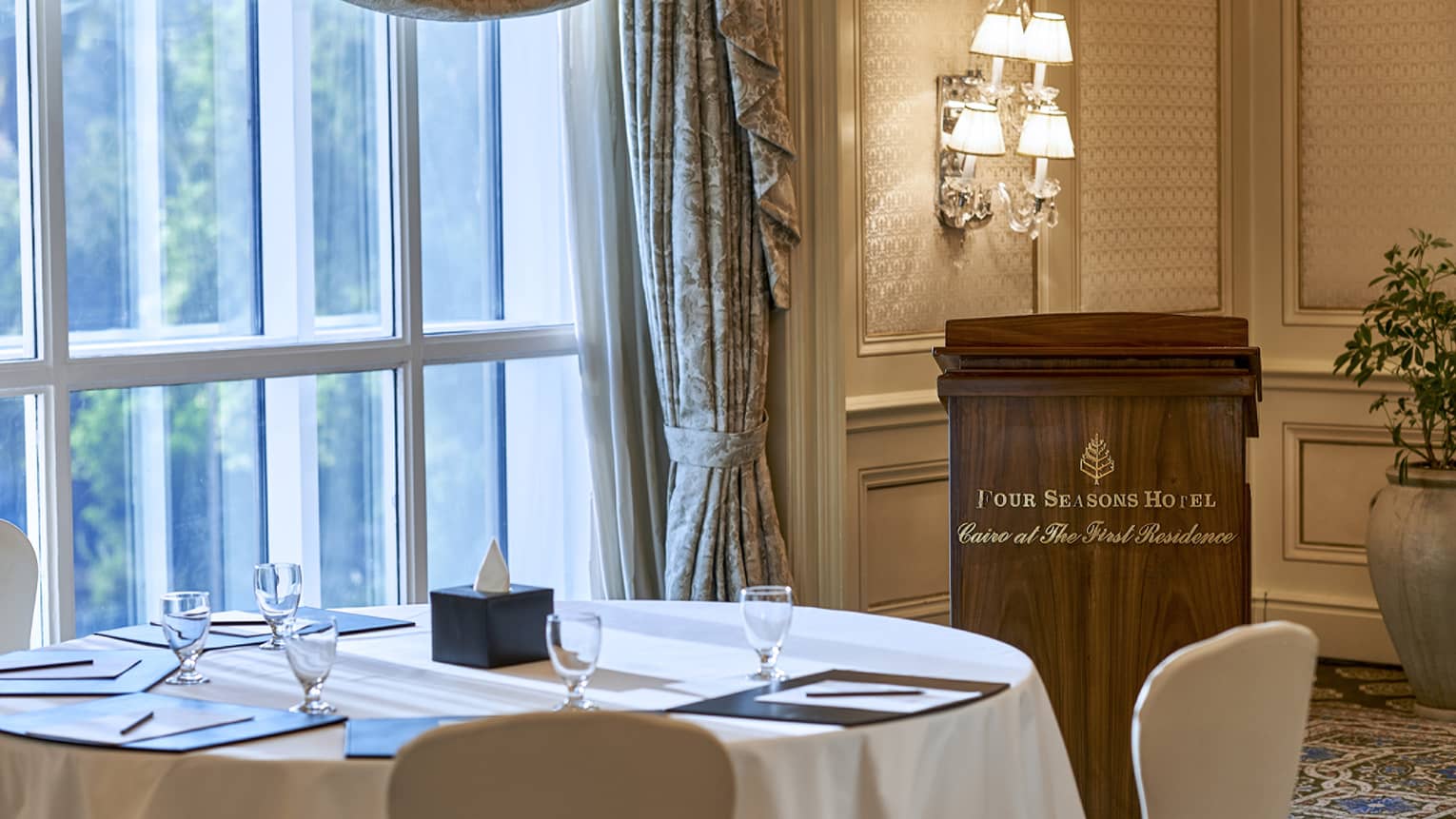 Round table by sunny window, speaker podium with Four Seasons Hotel Cairo at the First Residence logo