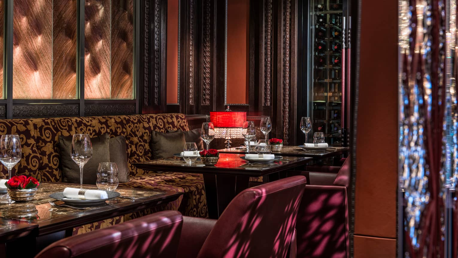 Brown decorative banquette along wall and red leather dining chairs around tables set with wine glasses
