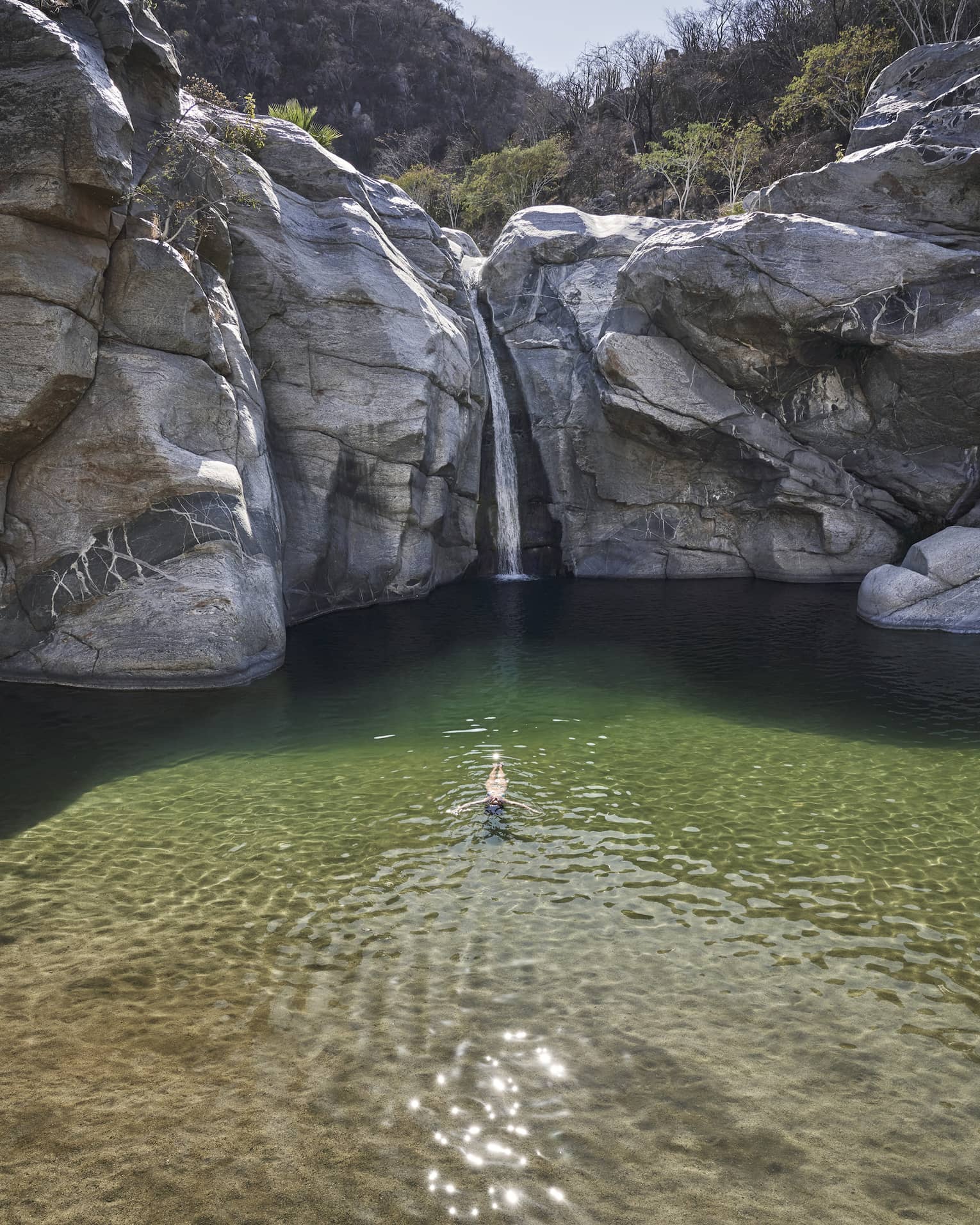 A person in a small well of water surrounded by large rock faces and trees.
