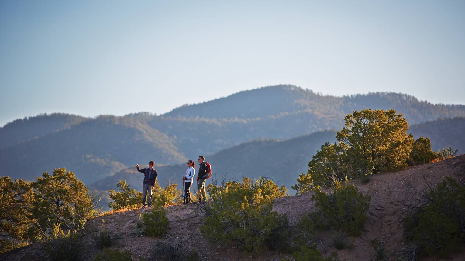 Three people hike on desert mountain hill