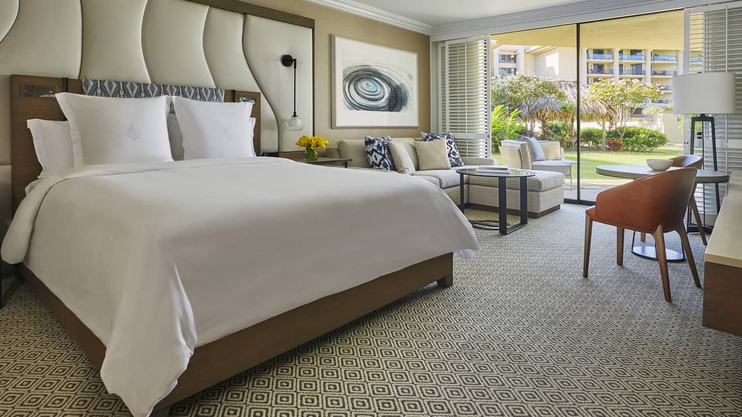 Guest room with king bed, seating area, desk and sliding doors opening to garden view and outdoor lounge chairs