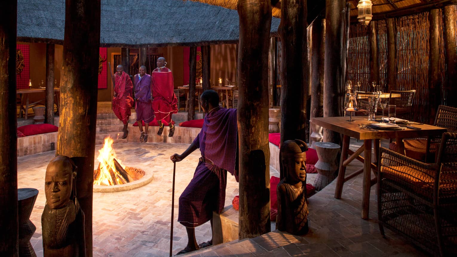 Maasai guides stand around open fire pit in middle of Boma Grill dining hut