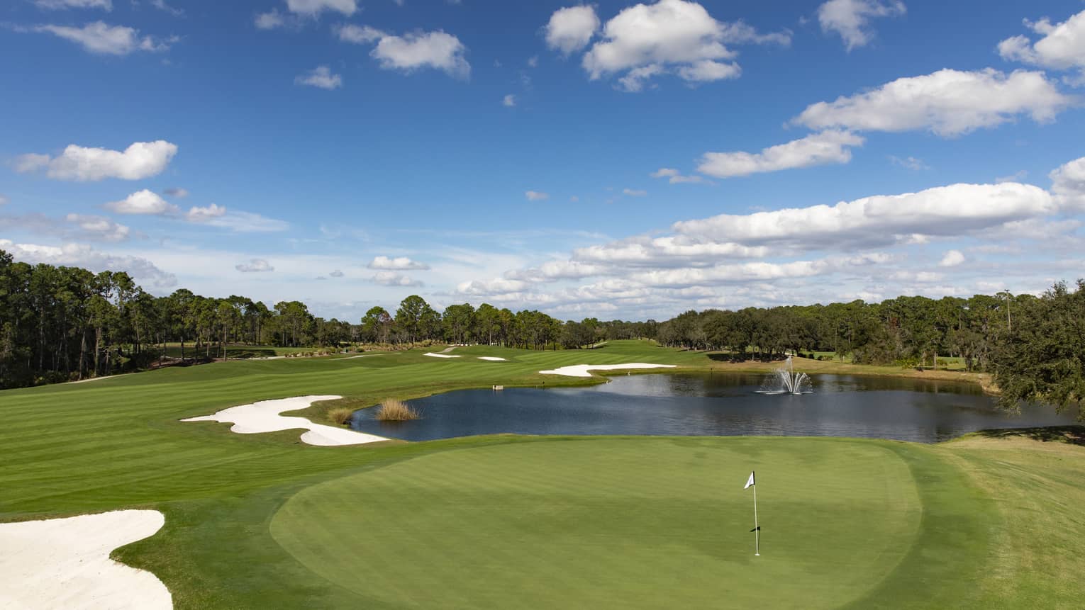 View across golf course green, small pond under blue sky 