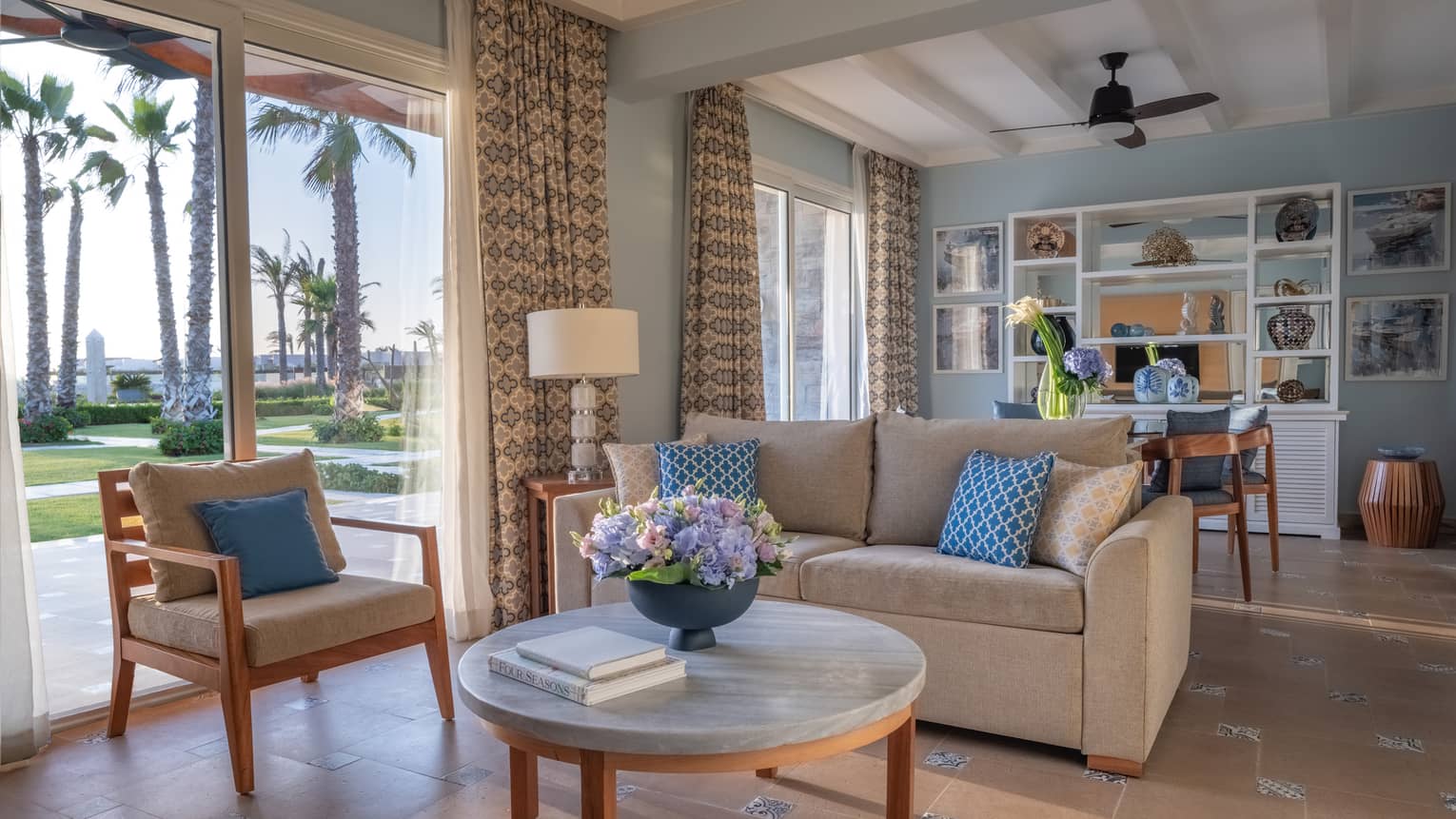 Guest room living area with tan sofa, armchair, round marble coffee table, dining table in background, sliding glass door to patio