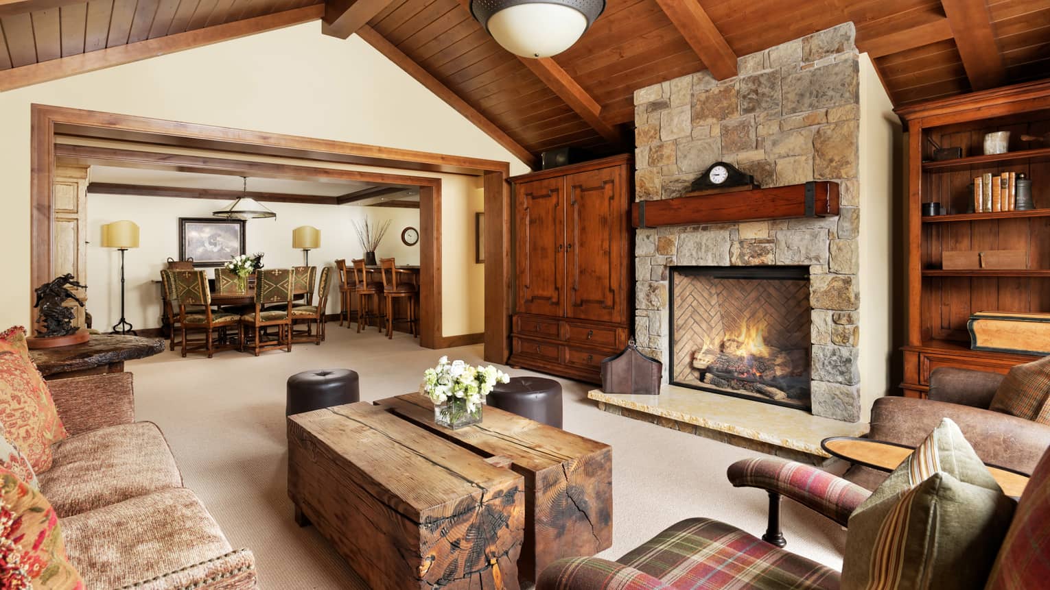 Large bright living room with stone fireplace,  wooden tables, upholstered coaches, wood trim