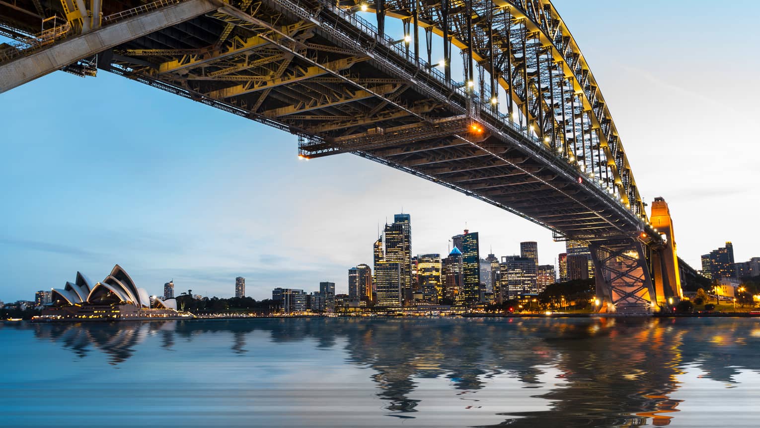 View from under bridge to Sydney waterfront skyline, lights at dusk