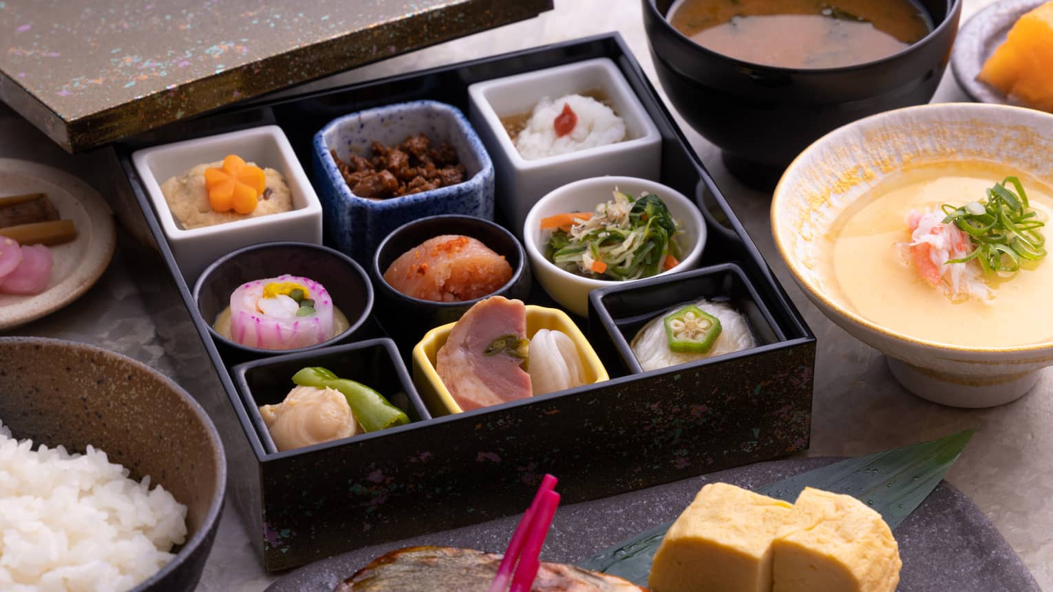 Traditional Japanese bento box breakfast with obanzai side dishes, tamagoyaki (Japanese rolled omelette), congee, steamed rice and miso soup