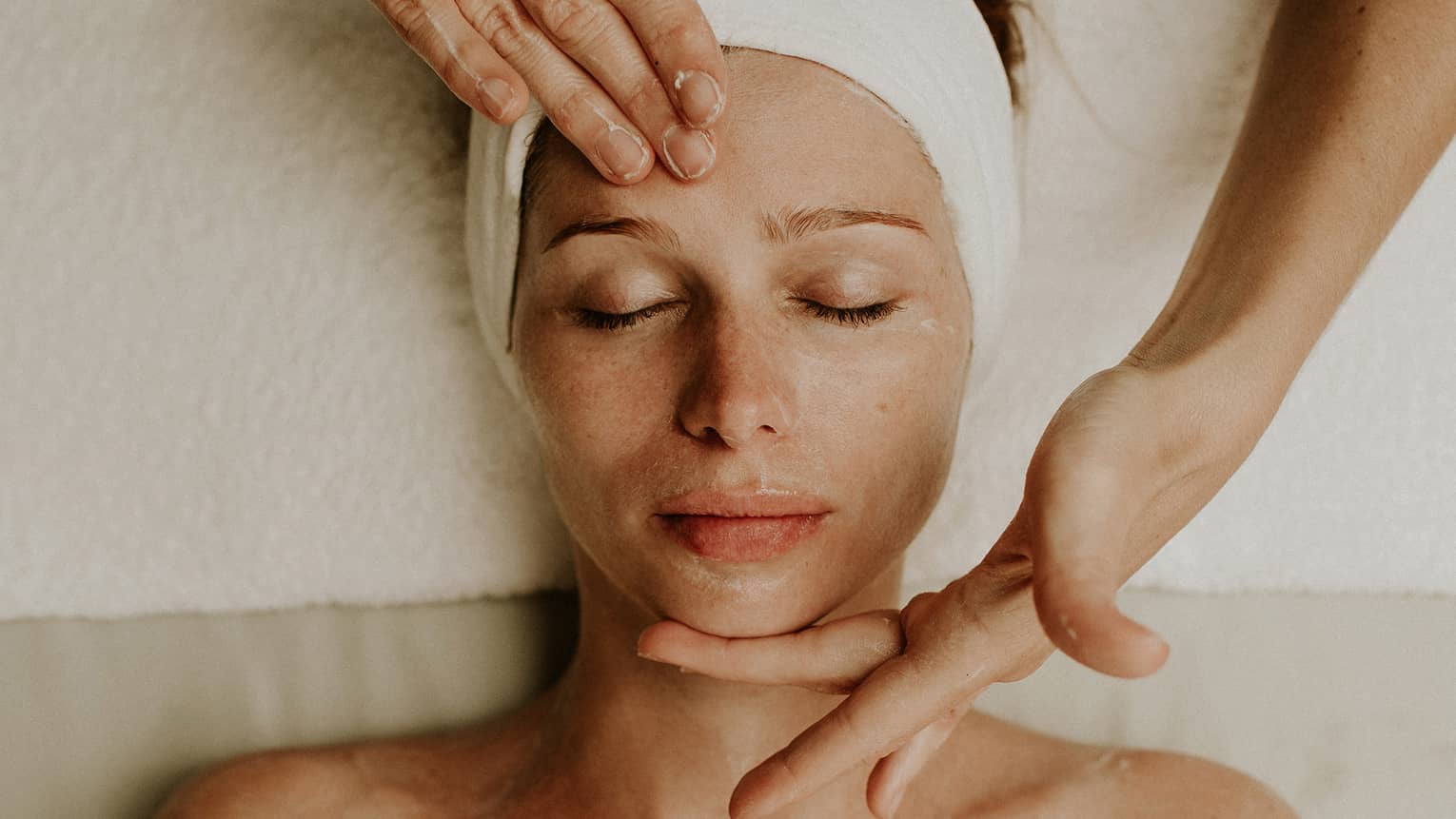 A woman reclines as a spa attendant performs a facial