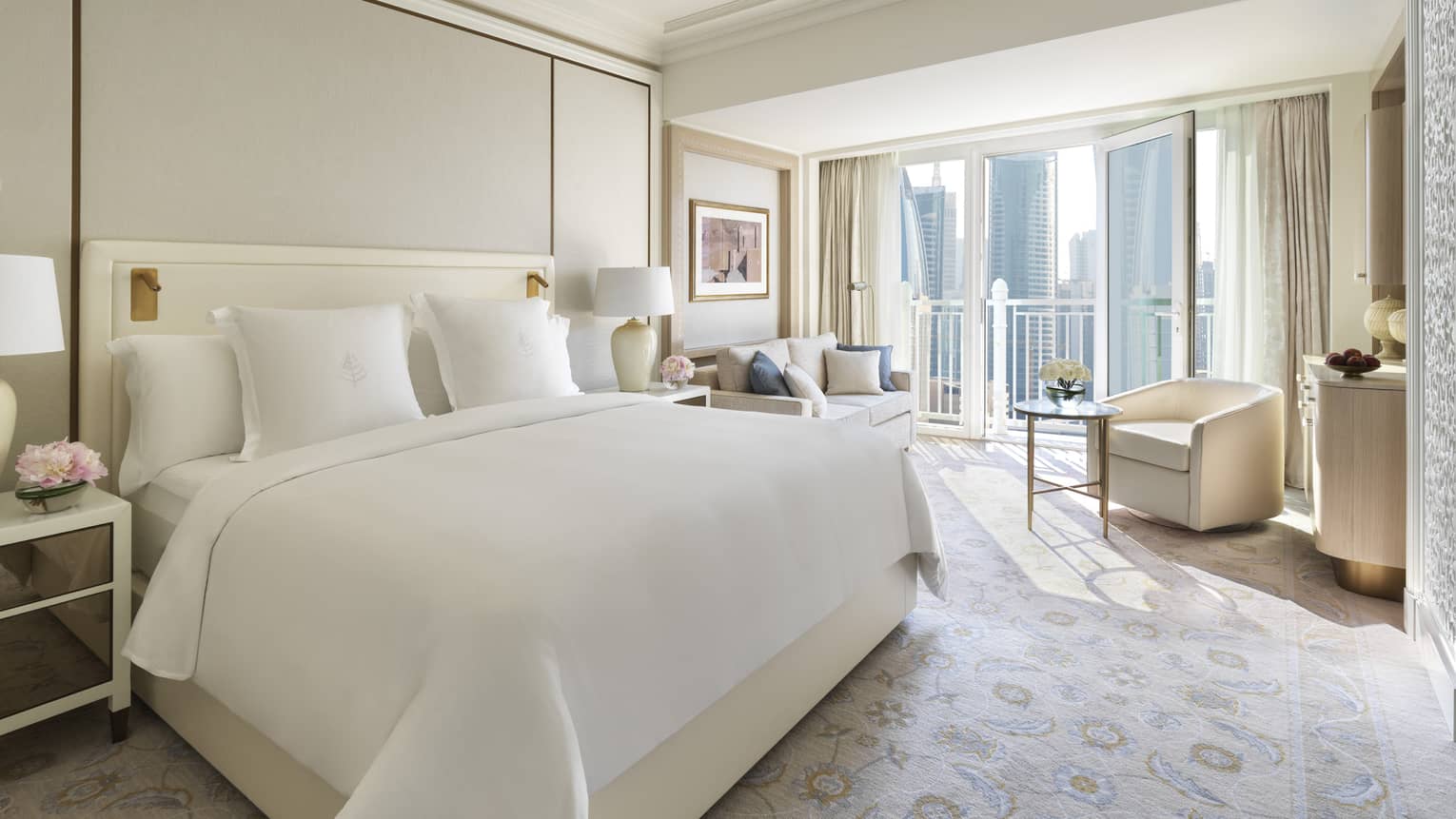 Hotel suite bed by armchair, table and sunny window with city view