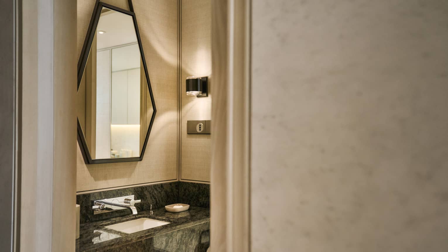 Looking into a hotel bathroom from the hallway ?�a sink and geometric mirror