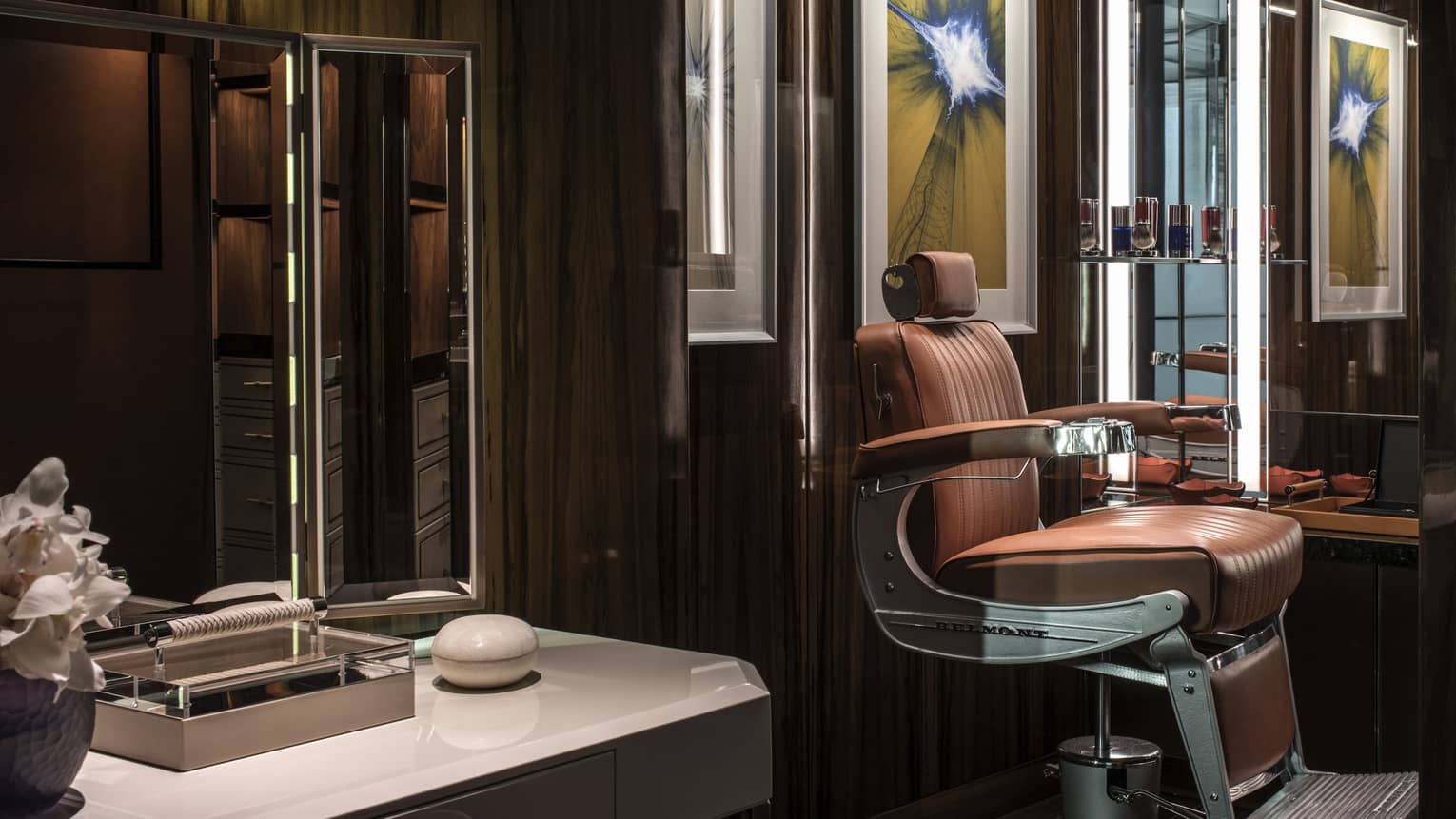 Brown leather barber chair, white counter with mirror in dimly-lit salon with dark walls