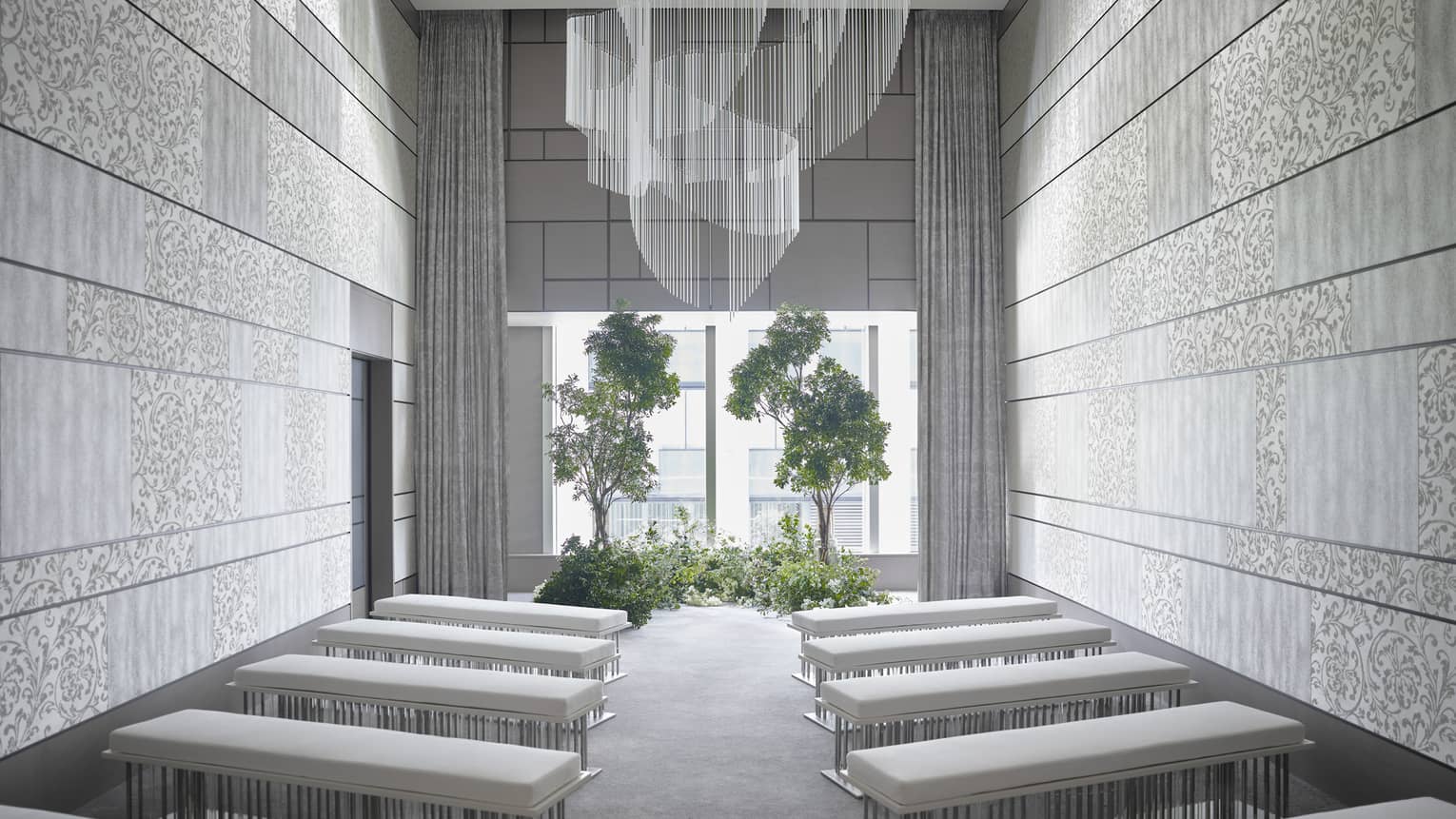 Modern event room, rows of plush benches face window and potted trees