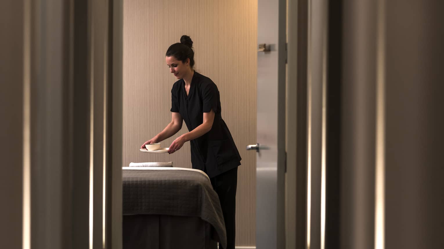 View through door as spa staff sets bowl on massage bed
