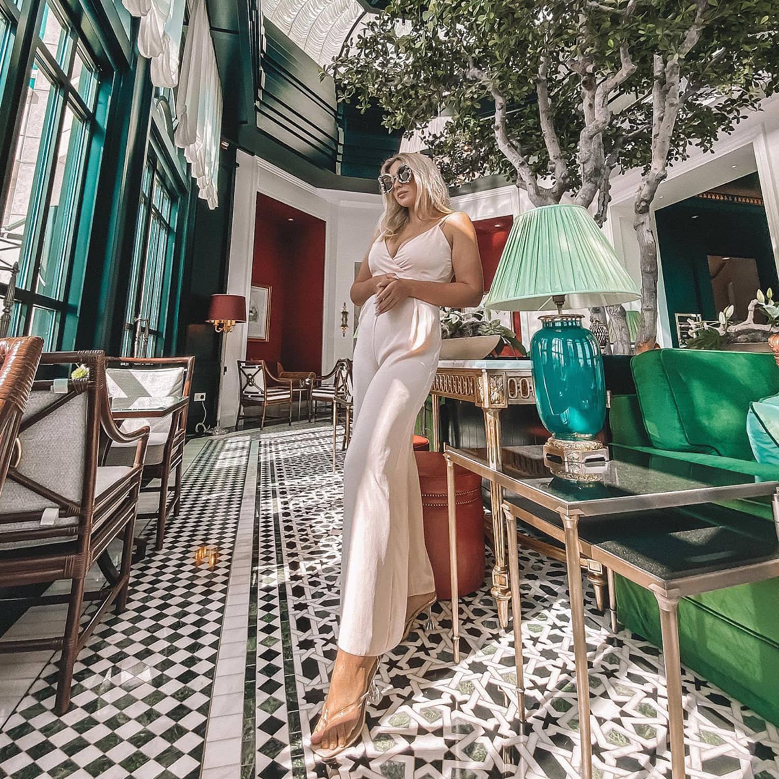 Women stands in lobby by lamp, sofa and potted tree