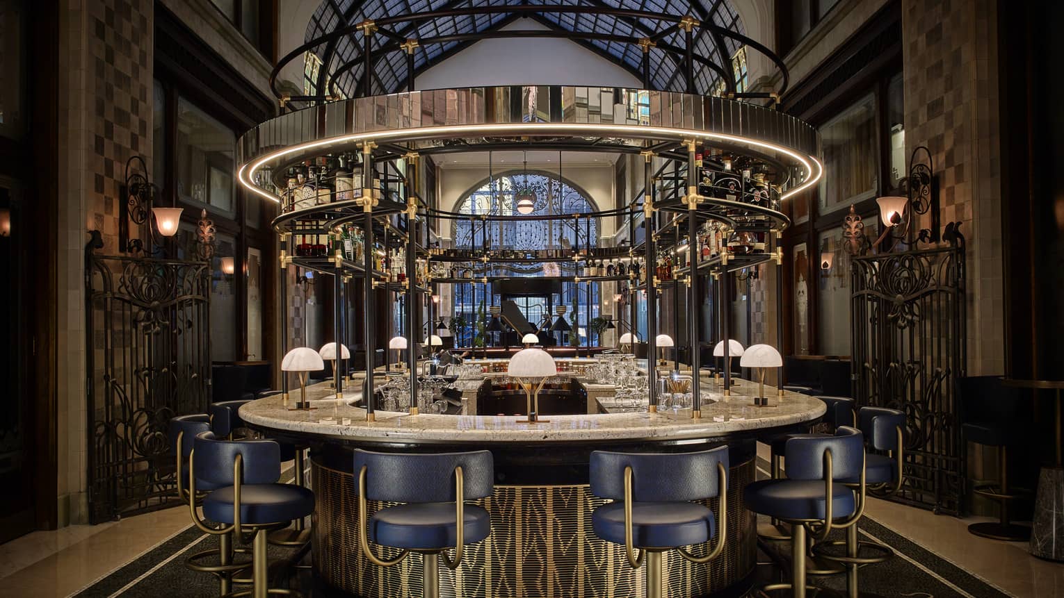 Elegant round bar with blue chairs and overhead glass rack in a grand interior space