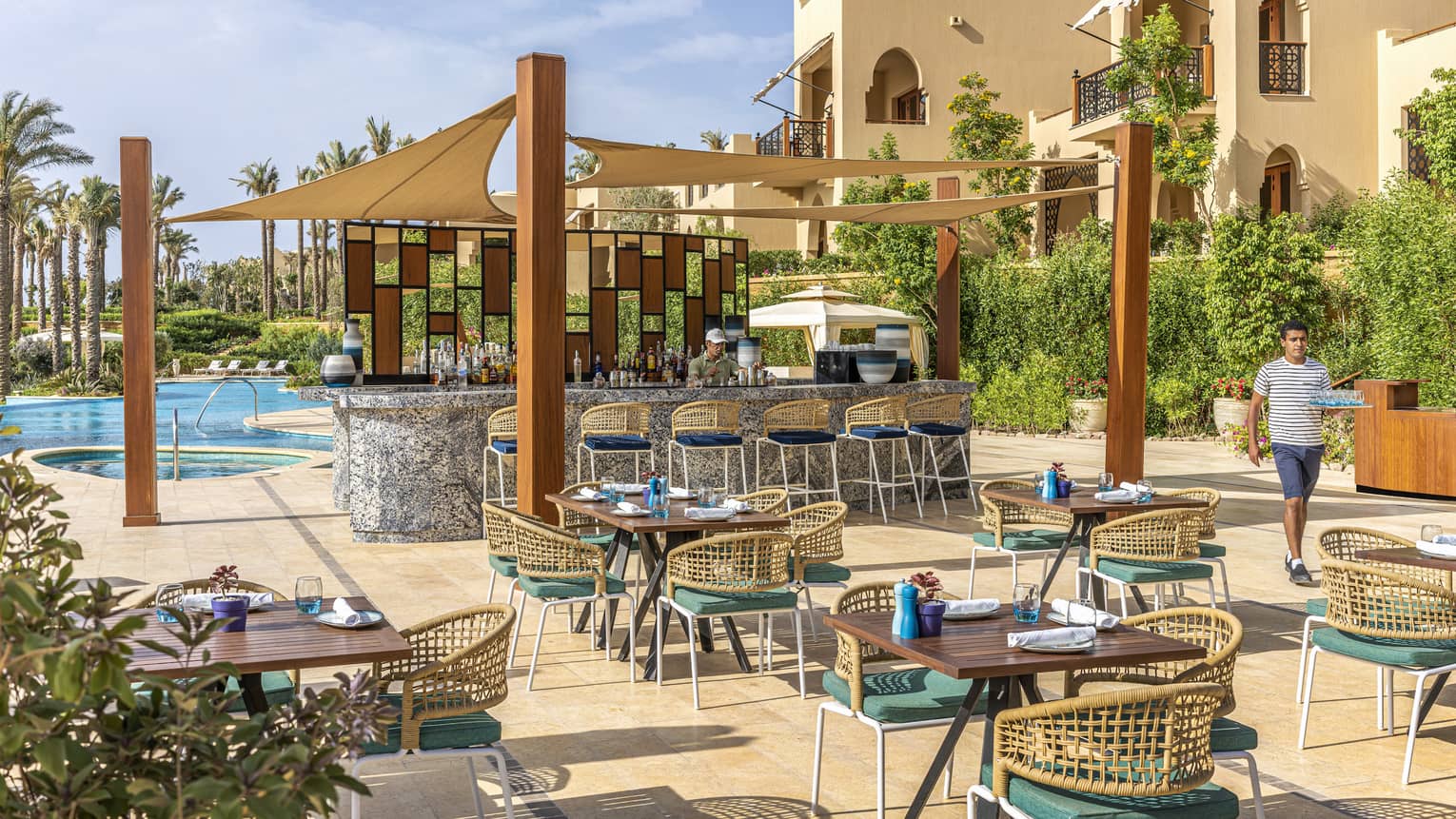 Poolside Luna restaurant with staff member walking past covered bar and intimate seating