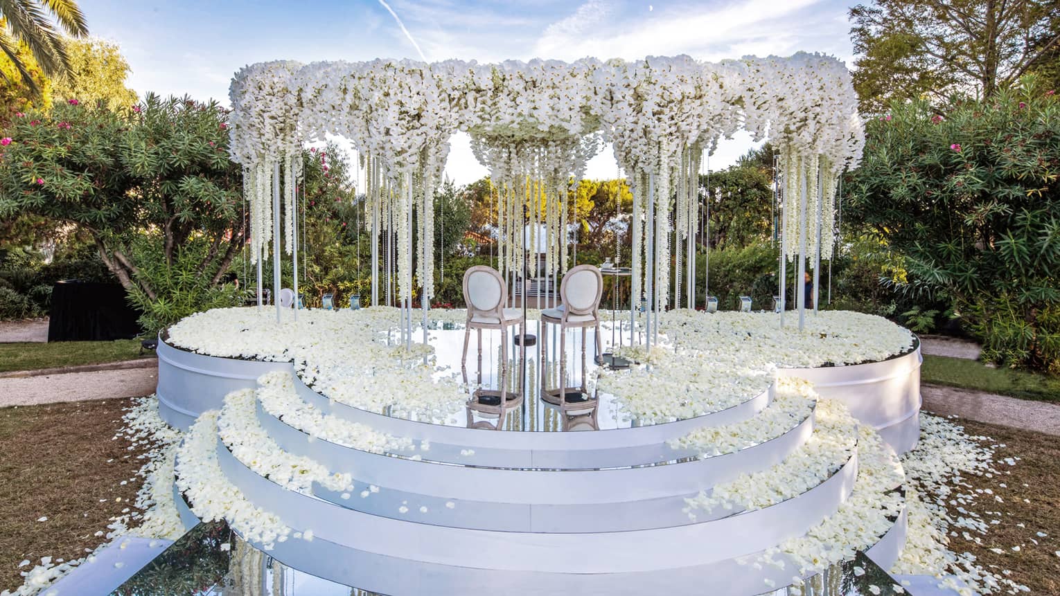 Three rounded white steps leading up to altar with arch covered in white flowers