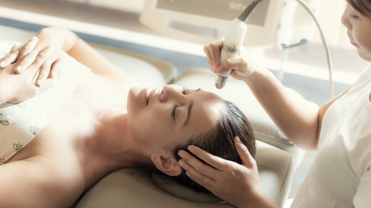 An aesthetician uses a tool on the face of a relaxing woman.