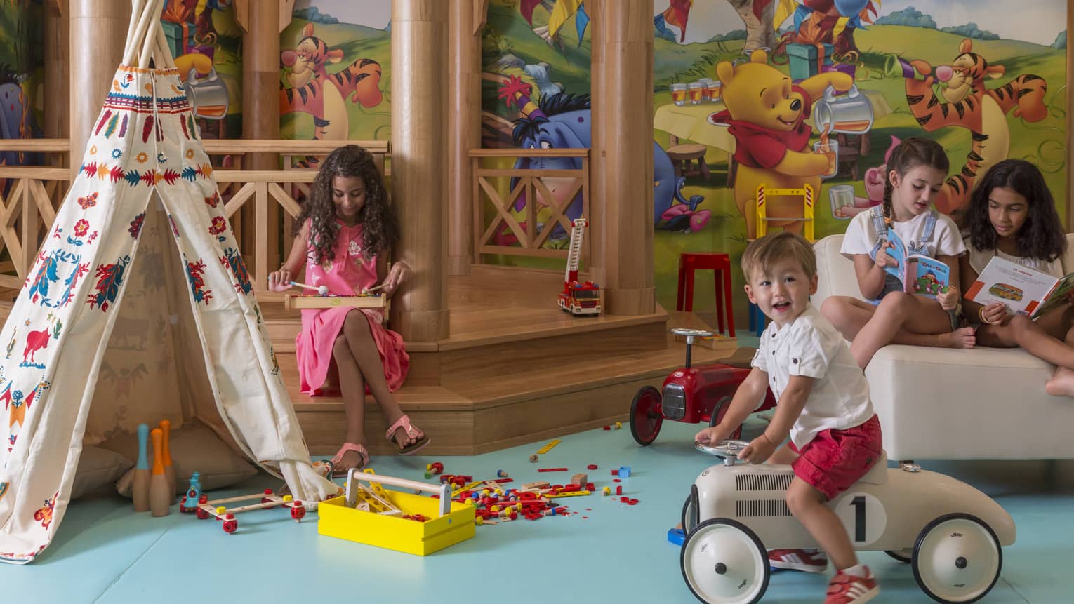 Two kids playing and two kids reading in colourful kids play area