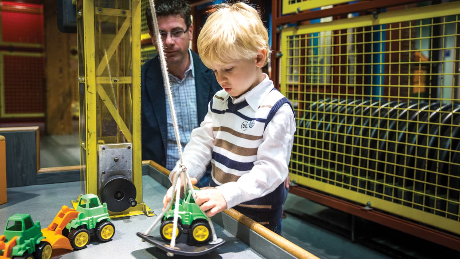 A small boy and father playing with toy trucks in a museum.