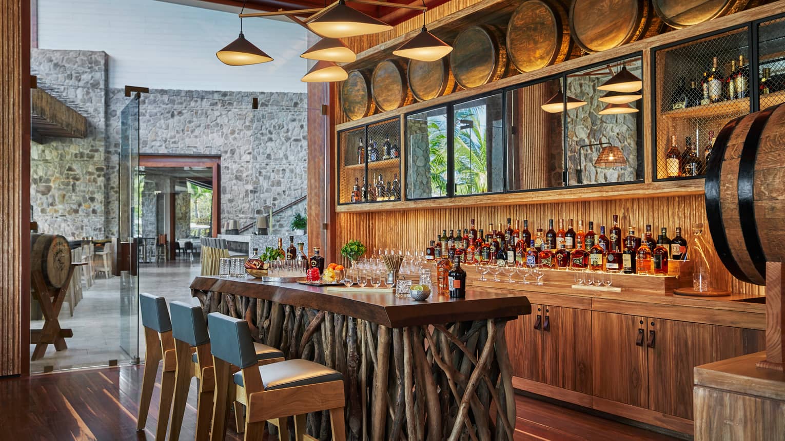 Modern chandelier above rustic wood tasting bar made from sticks, blue chairs, liquor display, barrel