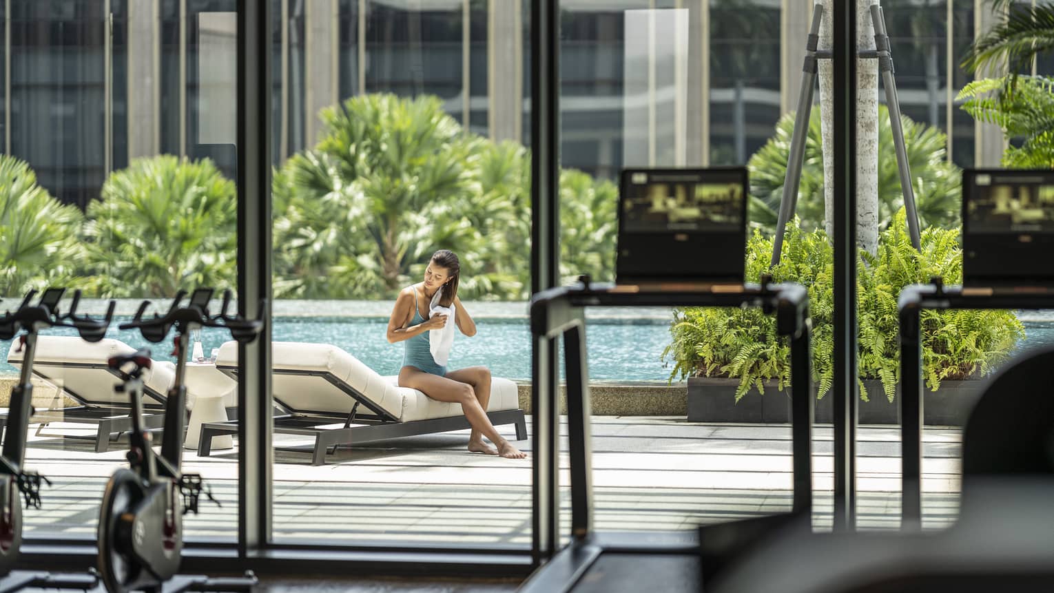 Woman sits on lounge chair as she towel dries her hair poolside