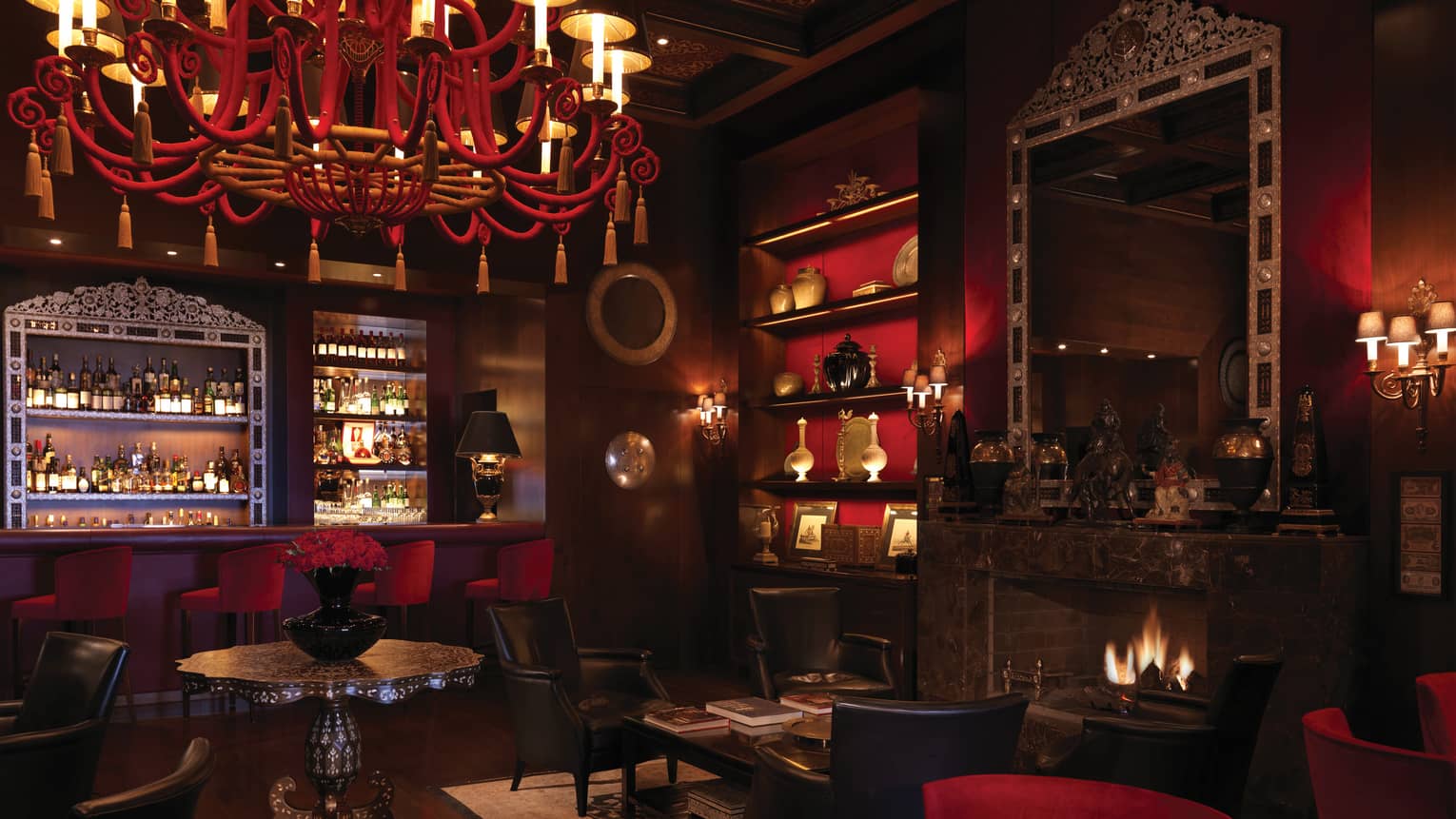 Bar interior with dark wood, red chandelier, shelf and velvet bar stools, arabesque ceiling, fireplace