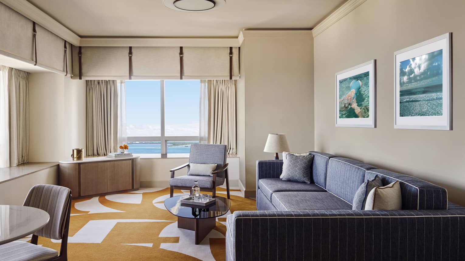Hotel suite living room with dark grey-blue sofa, orange and white carpet, arm chair and window with bay view