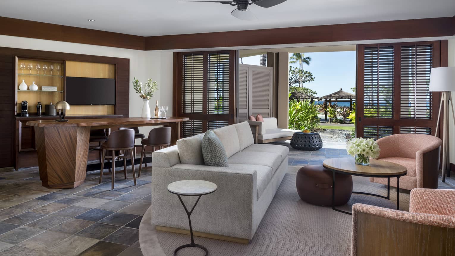 Suite's living room, with light grey sofa, two arm chairs, dining table, ceiling fan and walk-out terrace