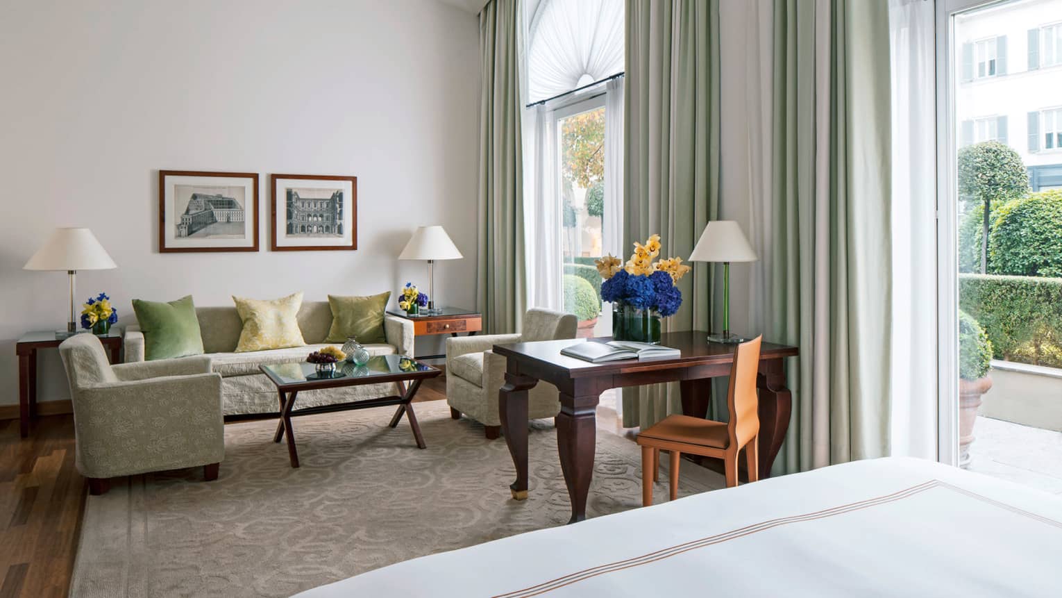 Junior Suite sofa, chairs, wood desk with flowers by two tall sunny windows